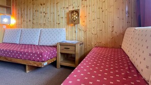 A wooden paneled room with two beds, a nightstand, a wall clock, and a framed picture. - Studio for 4 in Méribel Altiport, ski-in/ski-out, pets allowed (Méribel)