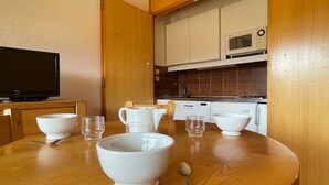 A dining area with a wooden table, white bowls, and a spoon. A television is on a wooden cabinet to the left. - Studio for 4 in Méribel Altiport, ski-in/ski-out, pets allowed (Méribel)