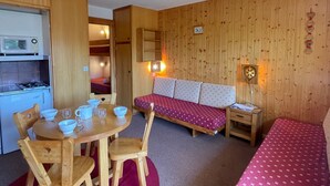 A compact room with a kitchenette, a dining table with chairs, a sofa, and a small bedside table with a lamp. - Studio for 4 in Méribel Altiport, ski-in/ski-out, pets allowed (Méribel)
