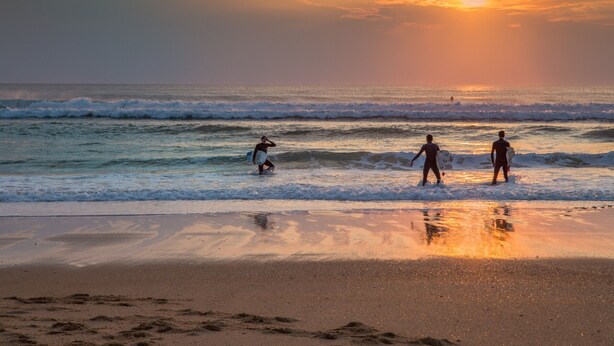 A beach scene with three surfers walking along the shore, carrying surfboards. - Beachfront Villa with Garden & Pool, 200m from Seignosse Beach (Seignosse)
