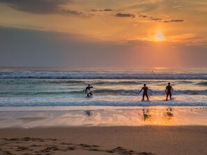 Eine Strandansicht, die drei Surfer beim Gehen am Ufer mit Surfbrettern zeigt.
