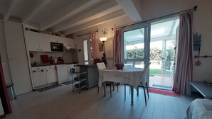 A compact kitchen with modern appliances, a dining area with a table and chairs, and a large sliding glass door leading to an outdoor area. - Beachfront Villa with Garden & Pool, 200m from Seignosse Beach (Seignosse)