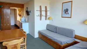 A compact room with a wooden dining table, a grey sofa, a small kitchenette, and a framed picture on the wall. - Ski-in/ski-out studio for 4 in Arc 1800 with balcony (Les Arcs 1800)