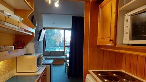 A compact kitchen with wooden cabinets, a microwave, a stove, and a small dining area with a sofa. - Ski-in/ski-out studio for 4 in Arc 1800 with balcony (Les Arcs 1800)