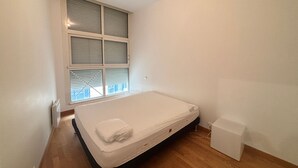 Ein kleines, sauberes Zimmer mit einem Einzelbett, einem Fenster mit Jalousien und Holzboden.