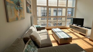 Ein modernes Wohnzimmer mit einer Couch, einem Couchtisch, einem Fernseher und großen Fenstern.