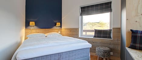 Une chambre à coucher avec un lit, deux lampes de chevet, une fenêtre donnant sur un beau paysage et un petit tabouret.