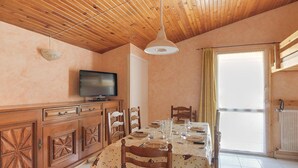 A dining area with a wooden ceiling, a television on a cabinet, and a table set for four.