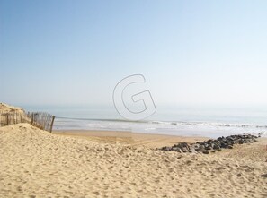 A beach with a sandy shore, a wooden fence, and a large 'G' watermark.