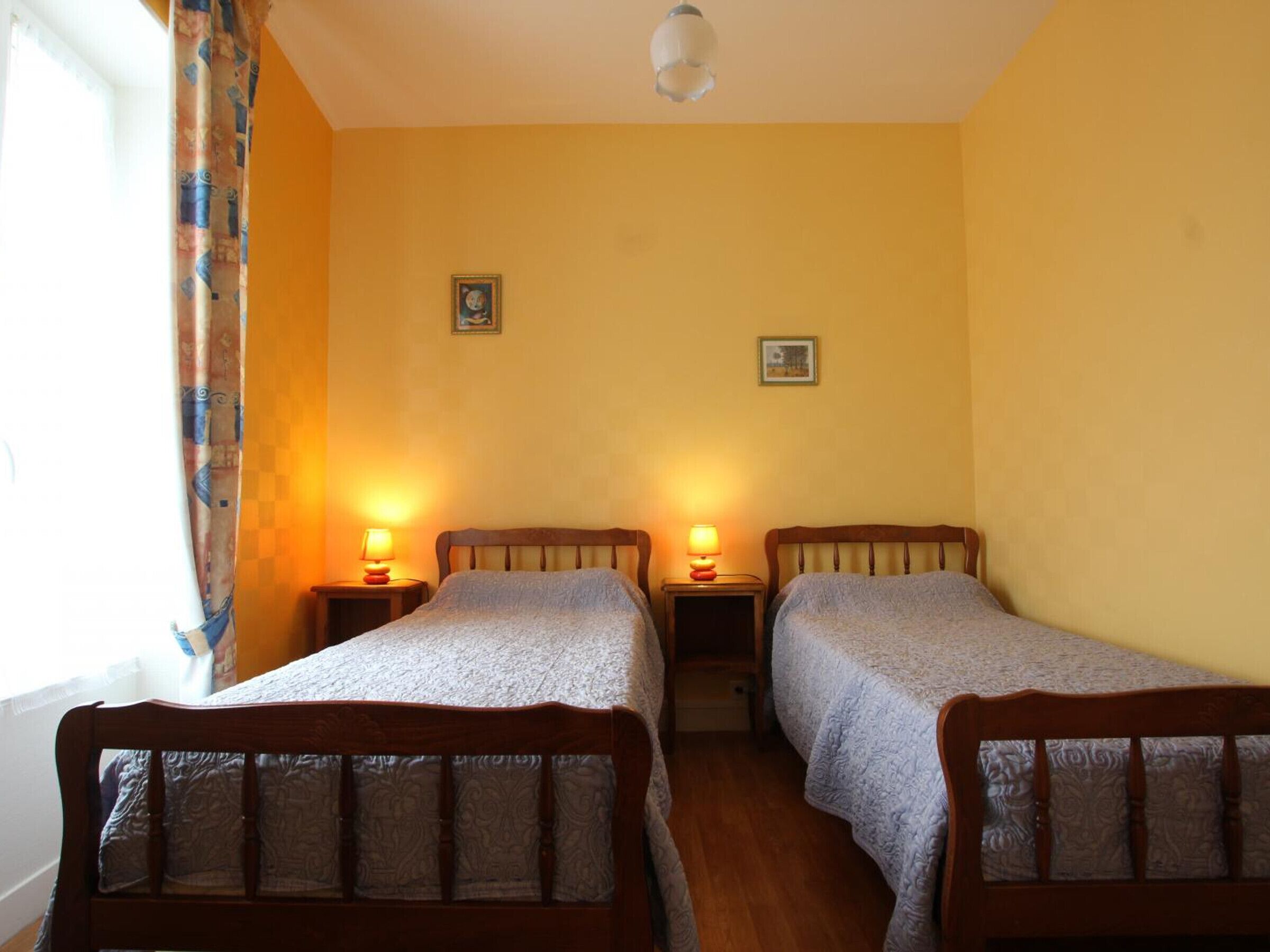 A room with two wooden beds, each with a headboard and a bedside table with a lamp.