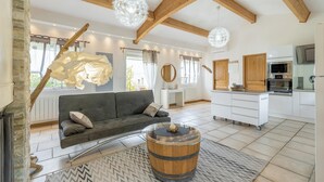 Una sala de estar moderna con un sofá, una mesa de centro tipo barril de madera y una zona de cocina con electrodomésticos.