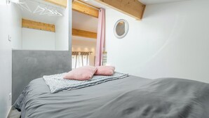 Un dormitorio con cama, techo de madera, un espejo y una ventana con cortinas.