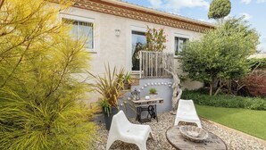 Una casa con un patio que tiene dos sillas de plástico blancas, una mesa de madera con una cesta y una planta en maceta.