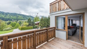 A balcony with a wooden railing overlooking a lush green landscape and a mountainous backdrop.