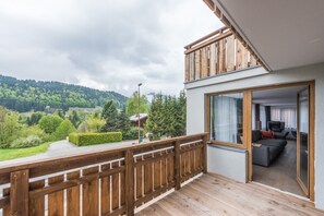 A balcony with a wooden railing overlooking a lush green landscape and a mountainous backdrop.