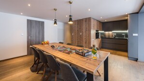 A modern kitchen with dark cabinets, a wooden dining table, and pendant lighting.