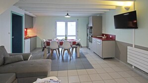 A compact living space with a dining area, kitchenette, and a flat-screen TV mounted on the wall. - Cozy cottage near the beach, wifi, pets allowed (Siouville-Hague)