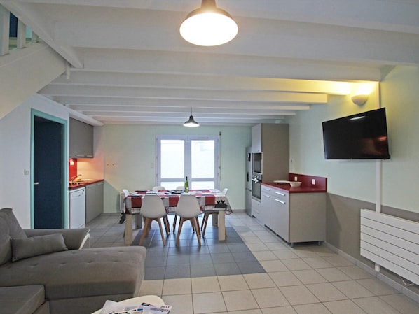 A compact living space with a dining area, kitchenette, and a flat-screen TV mounted on the wall.