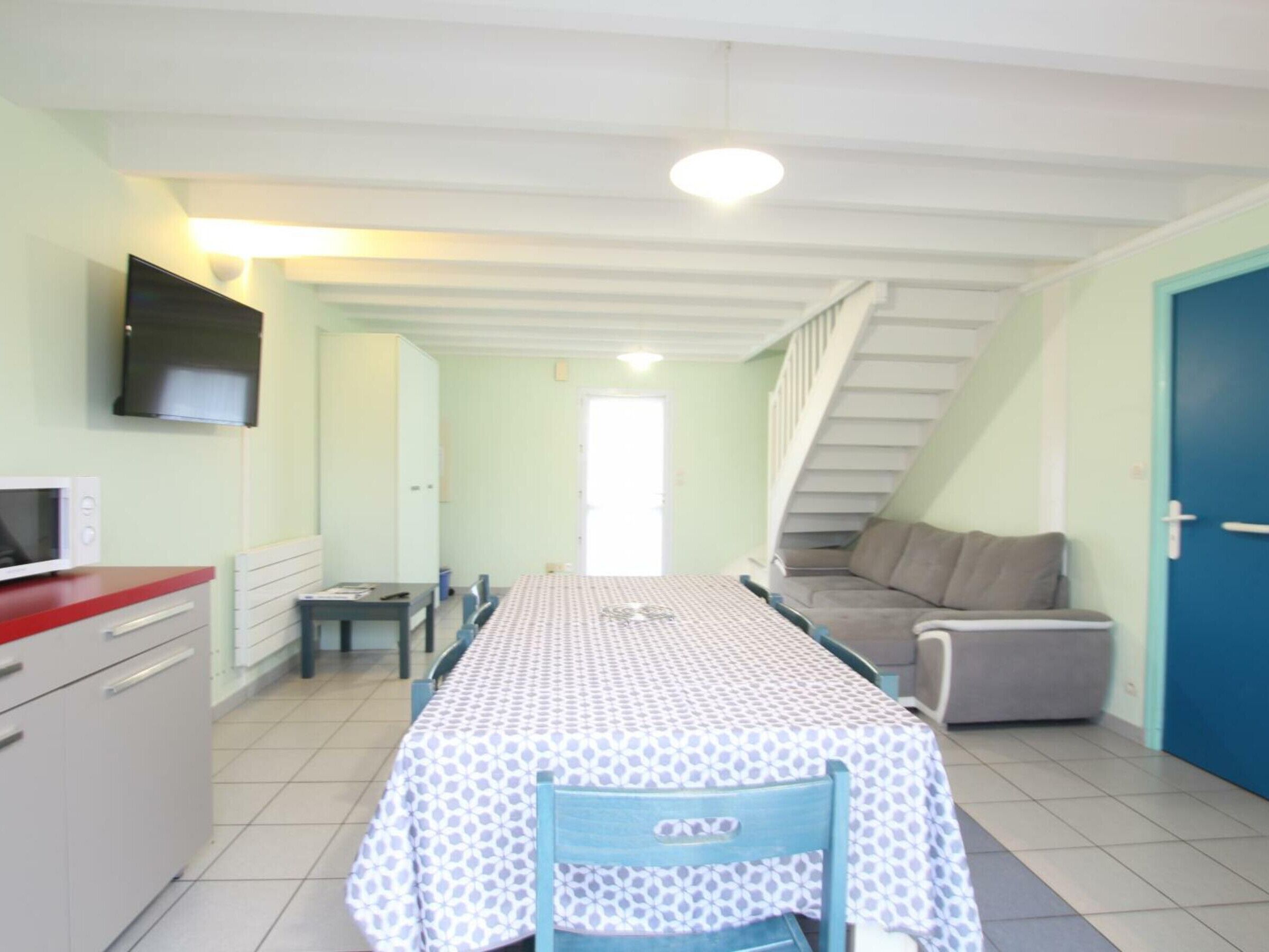 Una cocina compacta con comedor, un televisor montado en la pared y una escalera que conduce a un nivel superior.