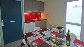 A compact kitchen with a red backsplash, a dishwasher, and a dining area with a table set for two. - Cozy cottage near the beach, wifi, pets allowed (Siouville-Hague)