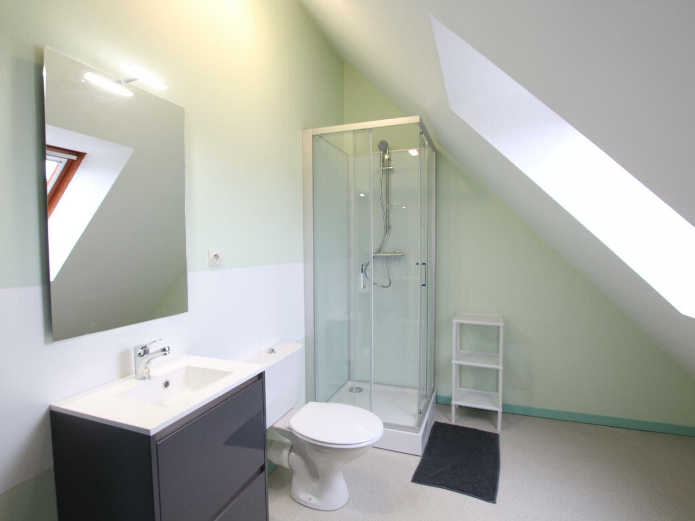 Un baño moderno con cabina de ducha de vidrio, inodoro blanco y tocador con espejo.