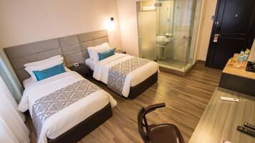 Habitación de hotel con dos camas, zona de ducha, escritorio con silla y un control remoto sobre el escritorio.