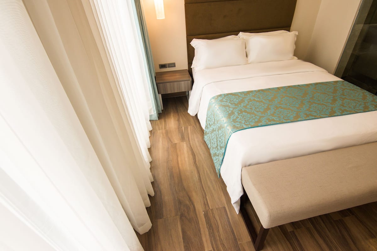 A hotel room with a wooden floor, a bed with a white and blue patterned bedspread, and a nightstand with a lamp.