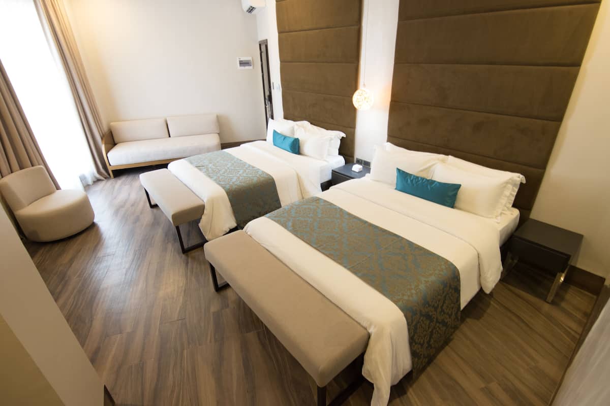 A hotel room with two beds, a sofa, a bench, and a nightstand with a lamp.