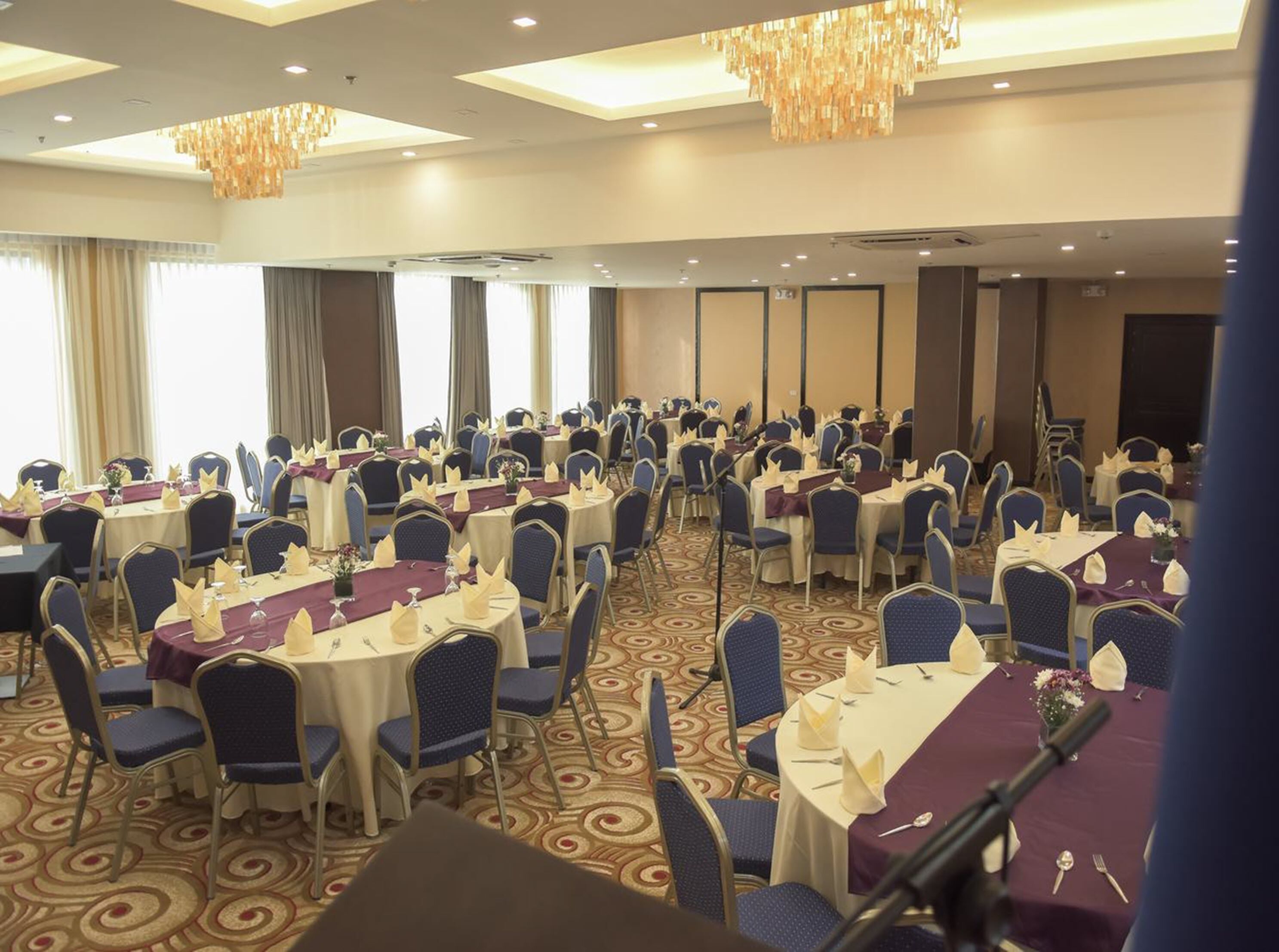A banquet hall with round tables and blue chairs, arranged in rows.