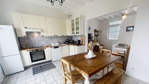 A kitchen with white cabinets, a wooden dining table, and a bench. - Charming Villa with Garden, Steps to Beach, Near Town, Free WiFi (Jullouville)