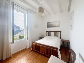 Une chambre à coucher avec un lit en bois, une fenêtre avec des rideaux, une table de chevet, une lampe et un tableau accroché au mur.