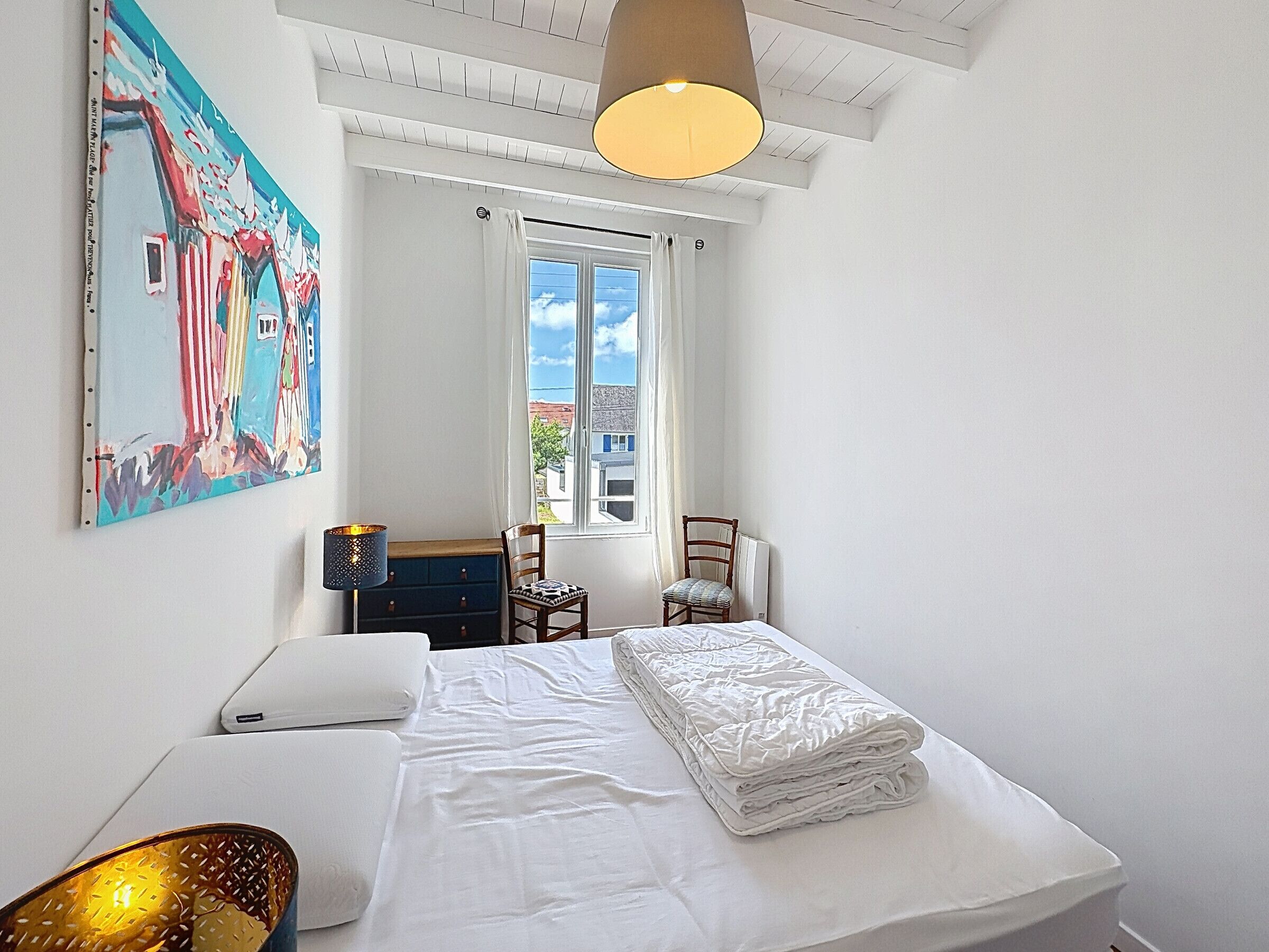 A bedroom with a bed, a chair, a desk, a window, and a painting on the wall.