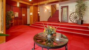 A lobby with a wooden ceiling, red carpet, a staircase, and a round glass table with a floral centerpiece.