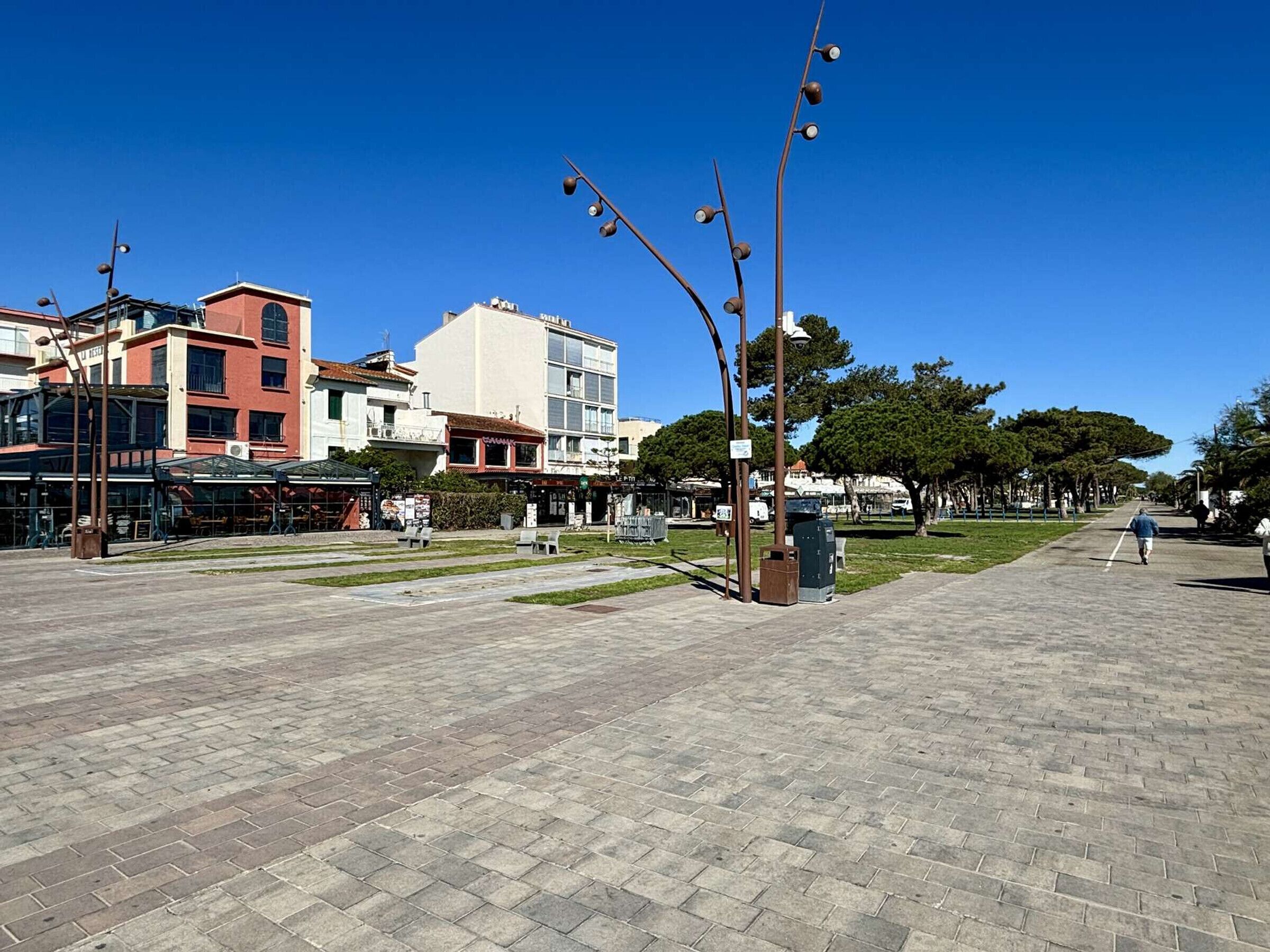 A paved pedestrian area with buildings, a street lamp, and a clear sky.