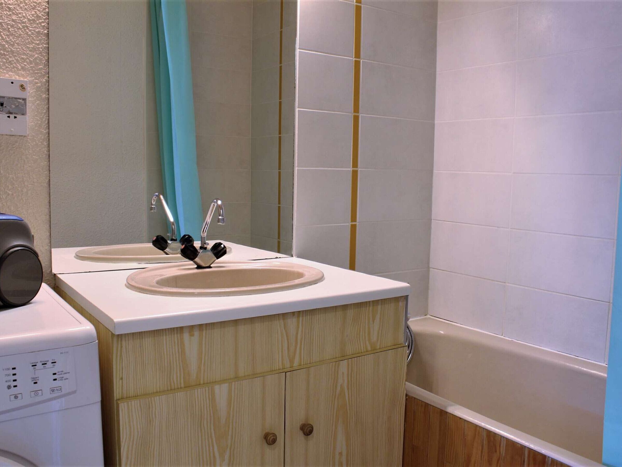 A bathroom with a double sink, wooden cabinets, a mirror, and a bathtub.
