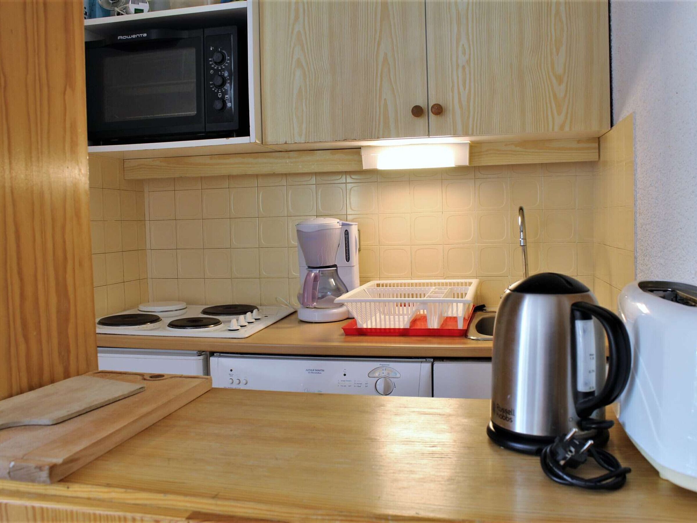 A kitchen with wooden cabinets, a microwave, a coffee maker, a kettle, and a toaster.