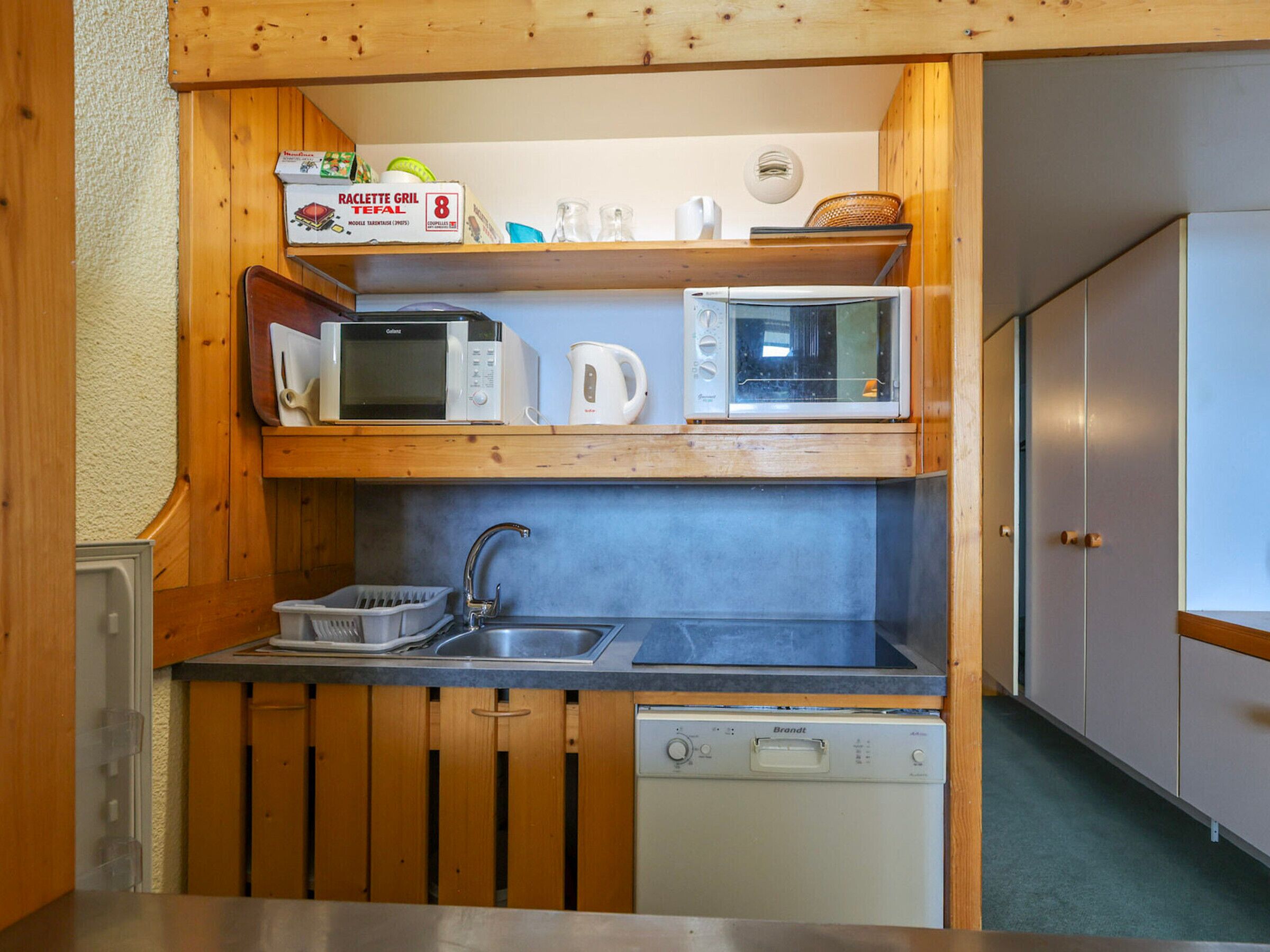A compact kitchen with wooden cabinets, a sink, and two microwaves.