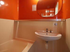 Un bagno con un lavandino bianco, uno specchio e una parete arancione.