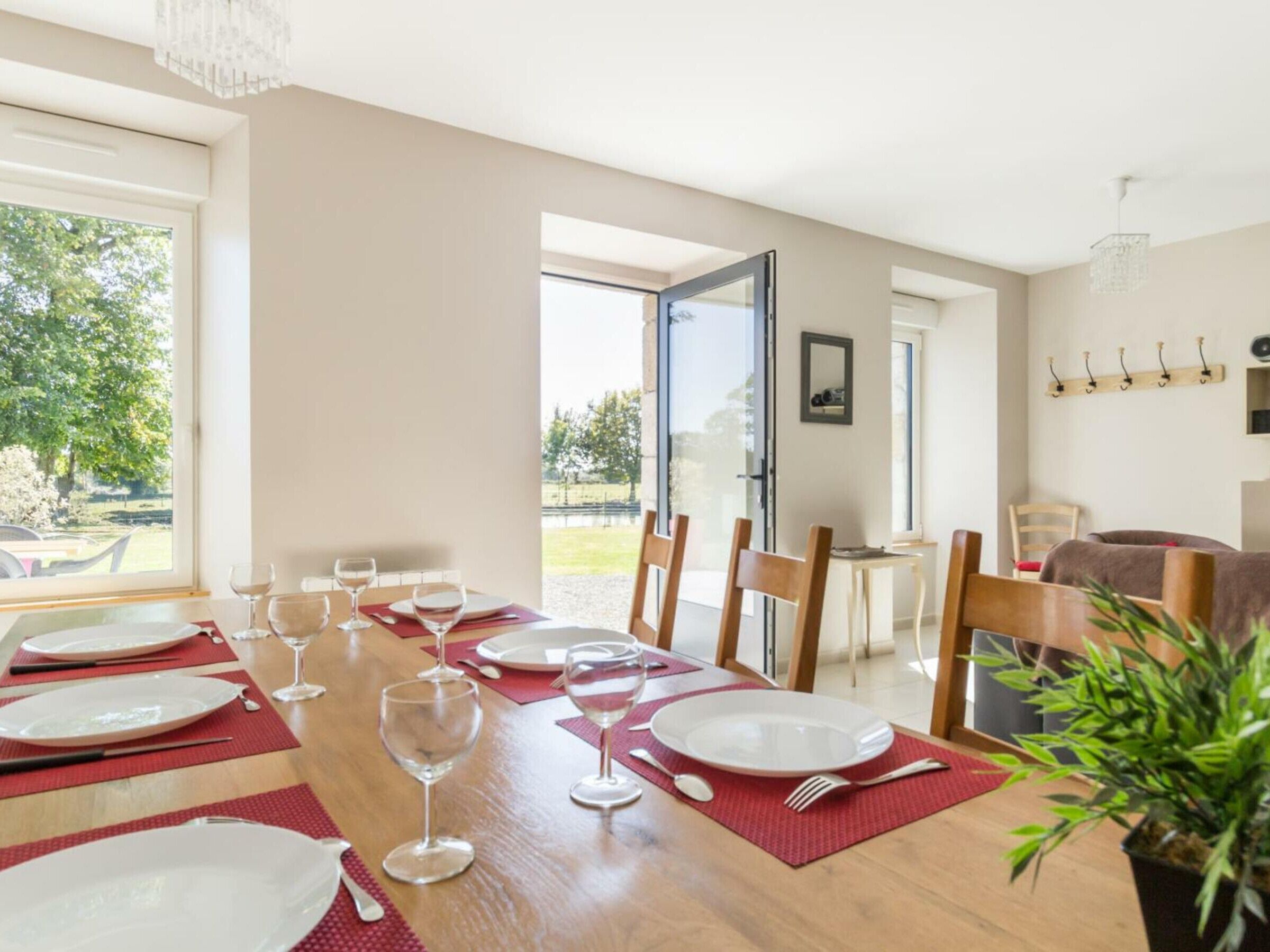 Zona pranzo con tavolo in legno apparecchiato per sei persone, ampie finestre e vista sull'esterno.