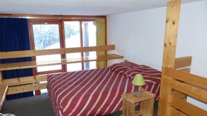 A small, single-bed room with a wooden bunk bed structure, a bedside table with a lamp, and a window with curtains. - Ski-in duplex for 5 in Charmettoger with WIFI (Les Arcs 1800)