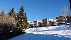 A snow-covered ski resort with wooden buildings, a ski slope, and trees. - Ski-in duplex for 5 in Charmettoger with WIFI (Les Arcs 1800)