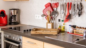 A kitchen with a stove, coffee maker, and various utensils on the wall. - Homerez - Spacious House in Gérardmer (Gérardmer)