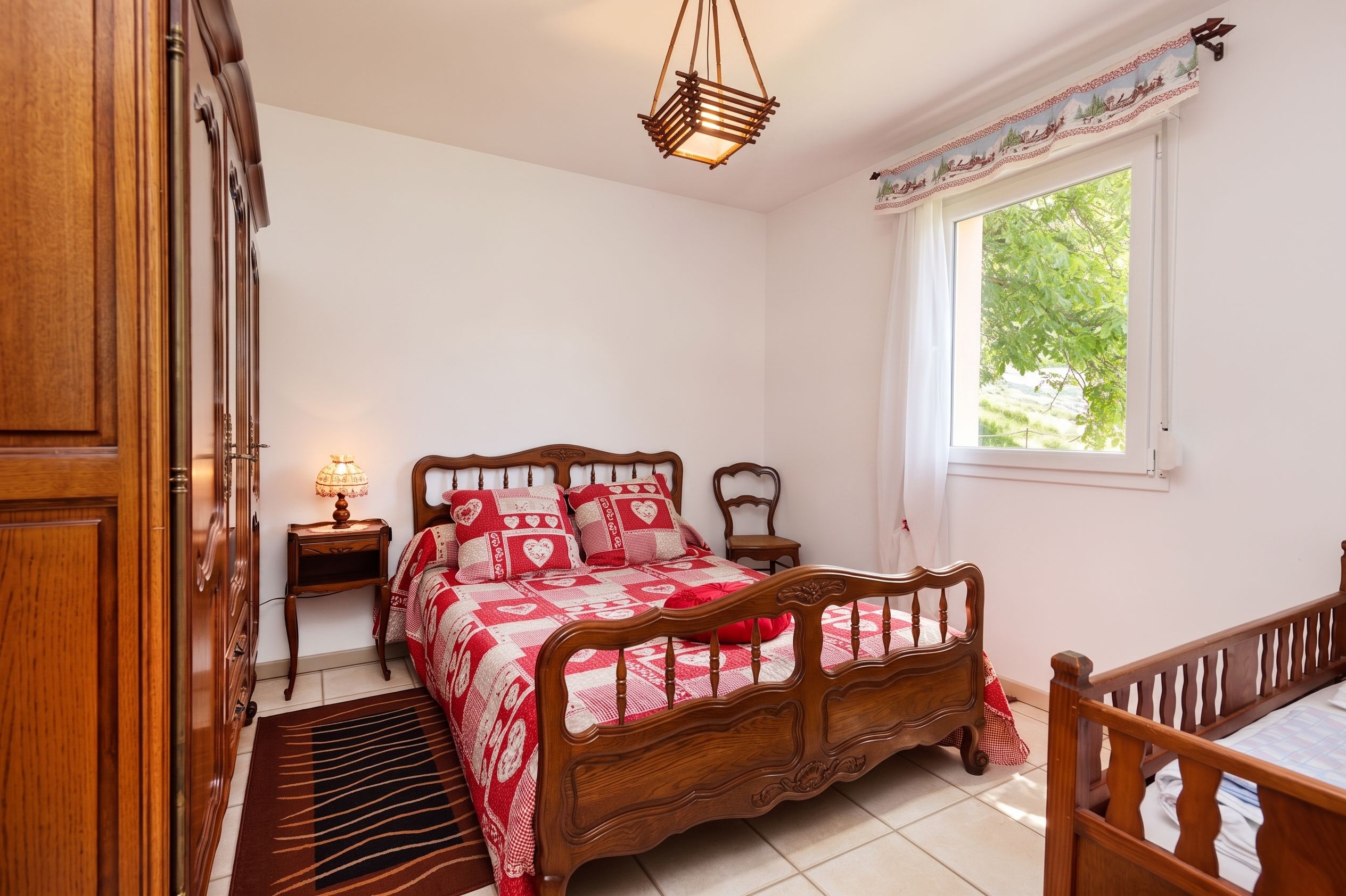 Une chambre à coucher avec un lit en bois, une table de chevet avec une lampe, une fenêtre avec des rideaux et une armoire en bois.