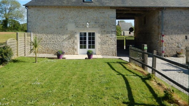 Un bâtiment en pierre doté d’une grande porte ouverte, d’une petite fenêtre et d’une pelouse verdoyante agrémentée de plantes en pot.