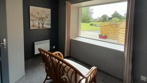 Une chambre moderne avec une grande fenêtre, un radiateur, une chaise en bois et un tableau accroché au mur.