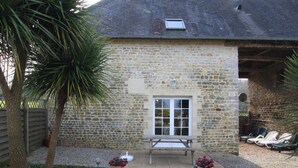 Un bâtiment en pierre doté d’un patio, d’un banc en bois et de deux plantes en pot.