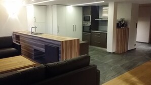 Una cocina moderna con electrodomésticos integrados, una zona de comedor con mesa de madera y un sofá, además de una pequeña kitchenette.