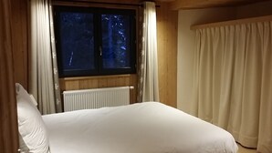 Un dormitorio con cama, ventana con cortinas, radiador y una cortina en la ventana.