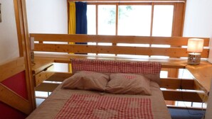 A wooden bed with a checkered bedspread and pillows, a nightstand with a lamp, and a window with curtains. - Duplex 2 Rooms - 5 Pers, Charmettoger Arc 1800, Pets Allowed (Les Arcs 1800)