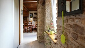 A narrow hallway with stone walls, wooden beams, a dining area in the background, and a clock on the wall. - Quiet house with garden and parking near Lessay (Laulne)